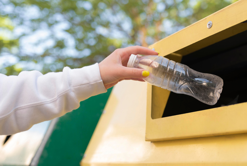 a hand putting a plastic bottle in a recycling bin